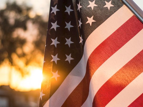 An American flag is pictured with a sun setting in the background, creating a warm and patriotic scene.