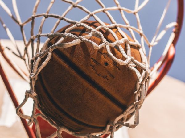 A basketball is captured in mid-air as it passes through a hoop, with the net and backboard visible against a blue sky.