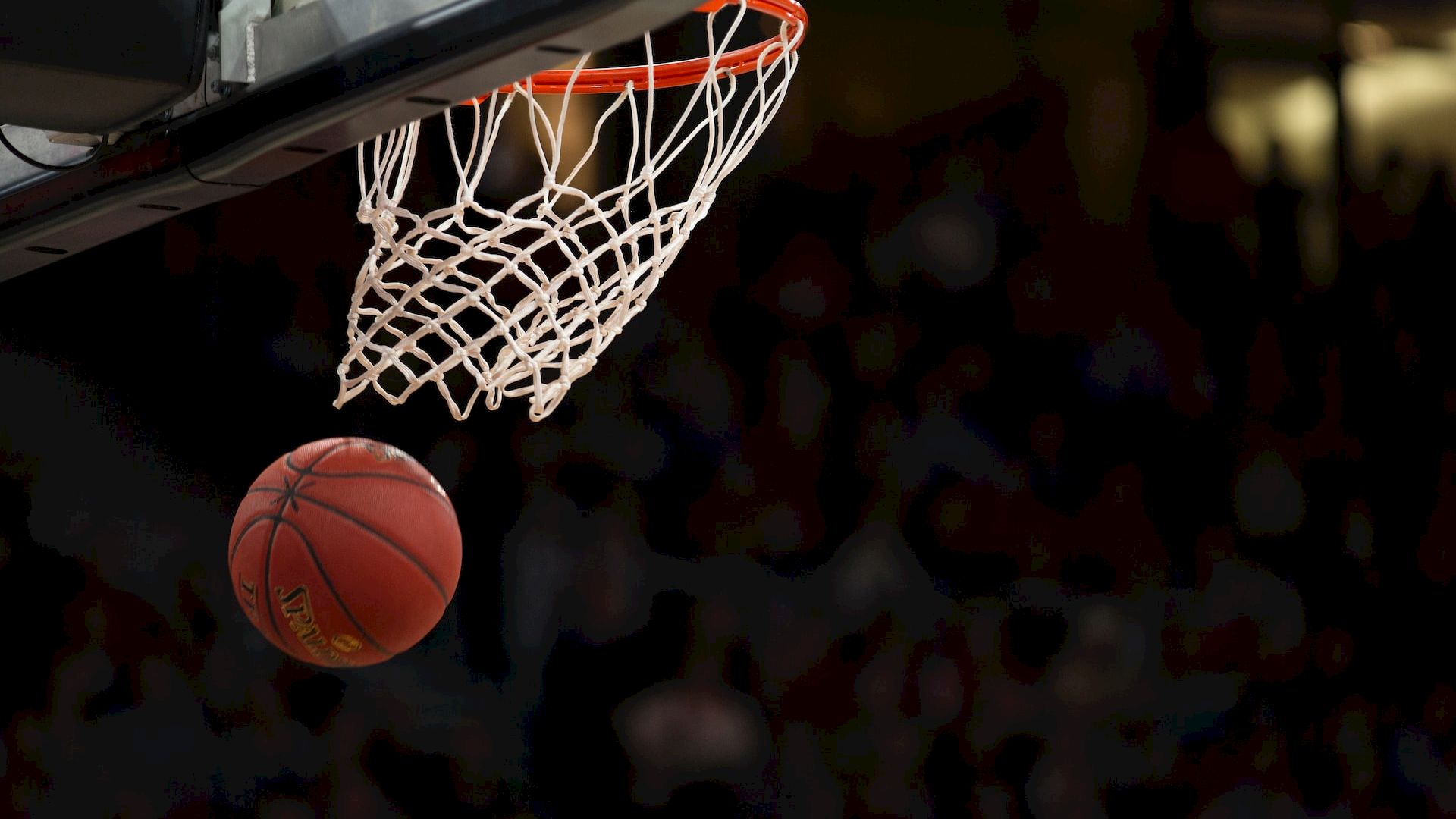A basketball is suspended in mid-air as it nears the hoop, ready to drop through the net in a sports arena.