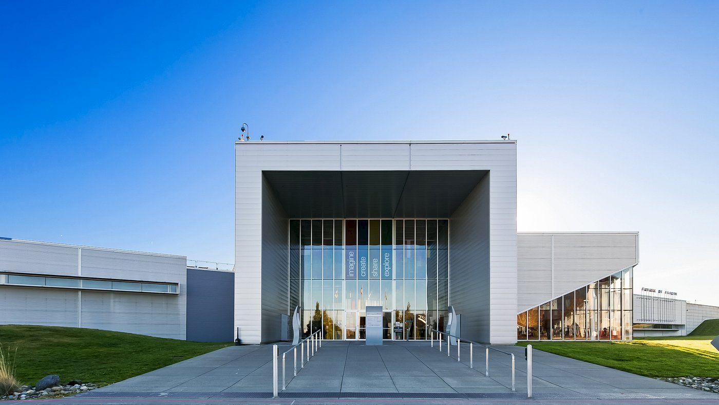 A modern, white building with large glass windows and a minimalist design, situated on a well-maintained lawn under a clear blue sky.