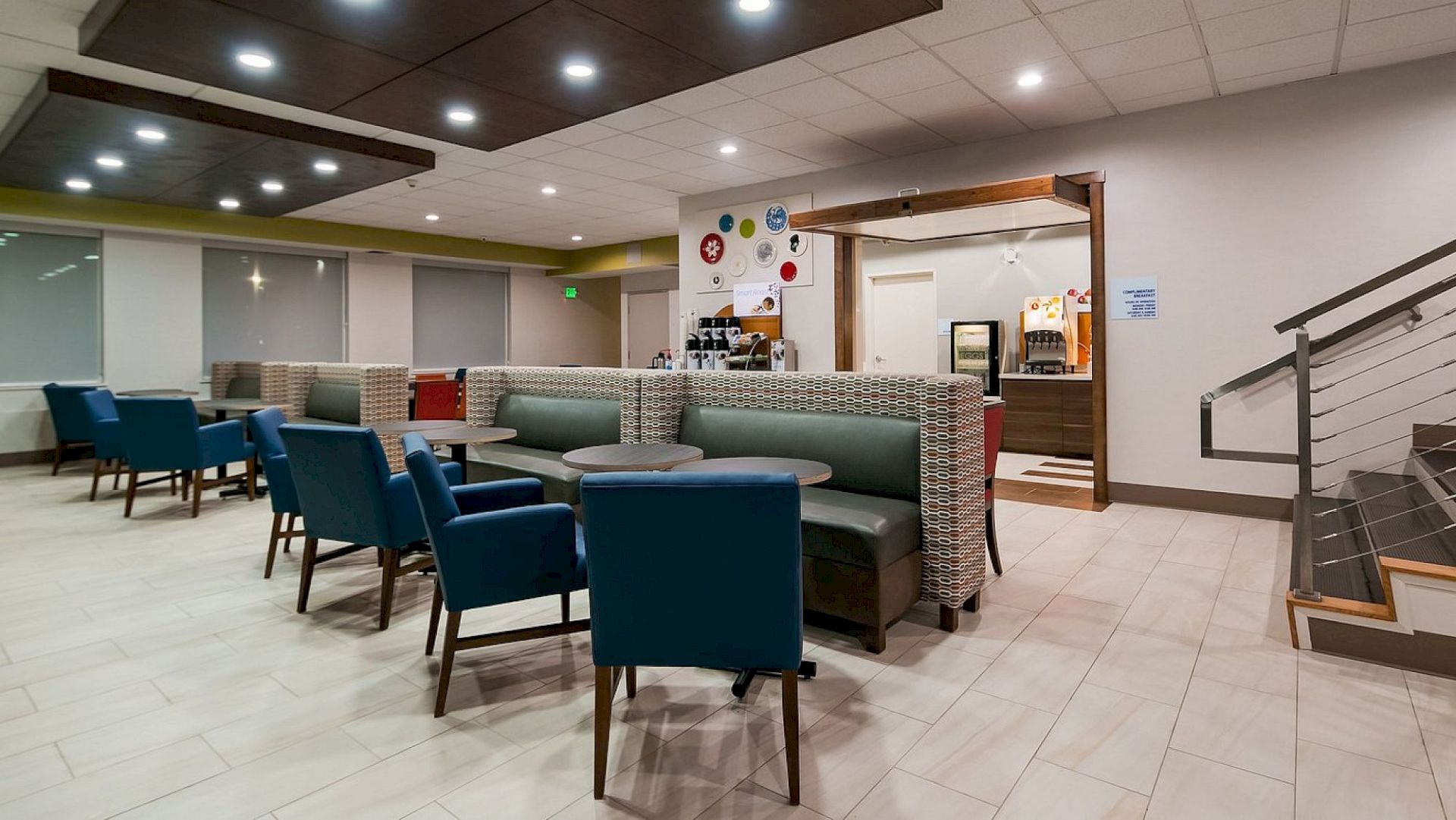 The image shows a modern, well-lit dining area with blue chairs, tables, and booth seating. A coffee station is visible in the background.