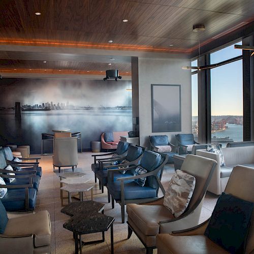 This image shows a modern lounge area with comfortable seating, large windows offering a scenic view, and artwork on the wall.