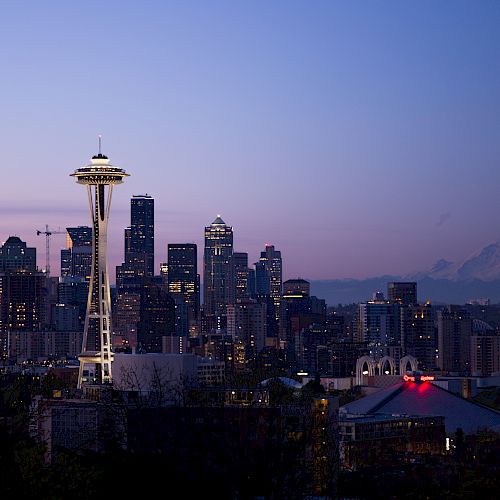 The image shows the Seattle skyline at dusk, with the Space Needle prominently visible and Mount Rainier in the background.