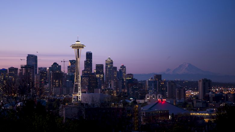 This image shows the Seattle skyline at dusk, featuring the Space Needle and mountains in the background. The sky has a beautiful gradient.
